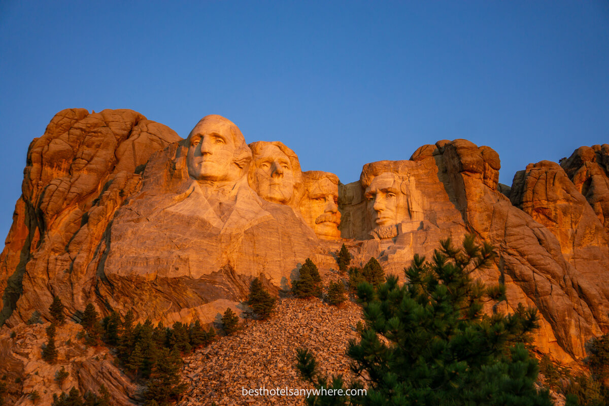 Mount Rushmore sculpture glowing orange at sunrise with a deep blue sky behind