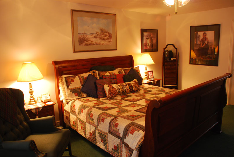 Inside a vintage guest bedroom with an author theme, large bed with sleigh frame and photos on the wall in a dimly lit room