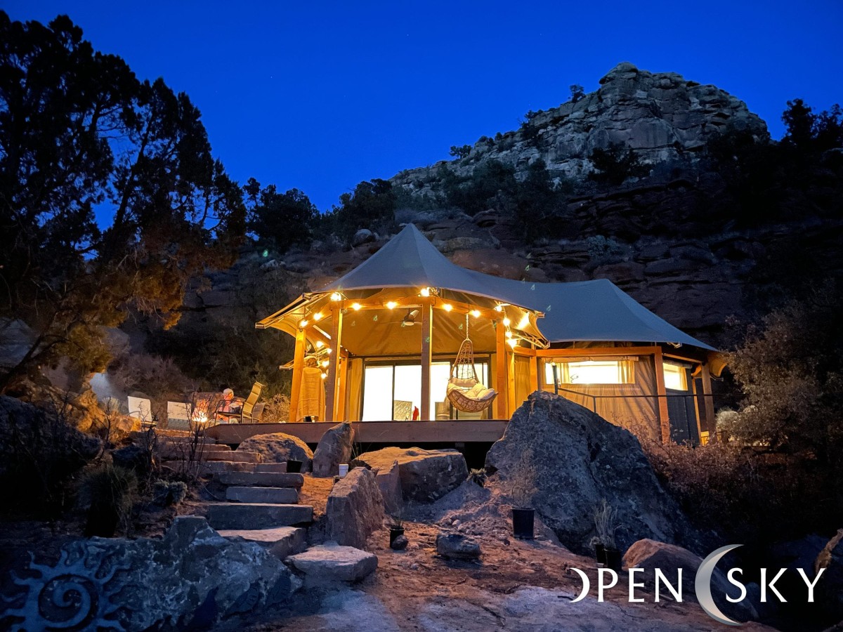 Photo of a luxury glamping yurt lit up at twilight with fairly lights and a rocky path leading to the structure