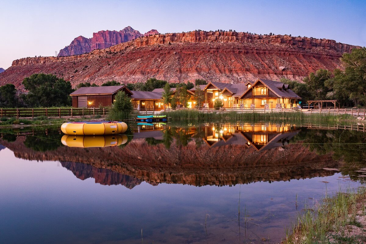 Photo of a wooden inn reflecting perfectly in still water with Zion's red rocks in the background at dawn