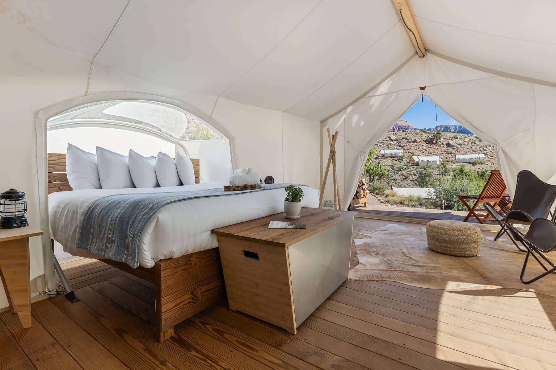 Inside a luxury white tent at Under Canvas glamping style Virgin UT hotel with bed, ottoman and chairs leading to deck with a view