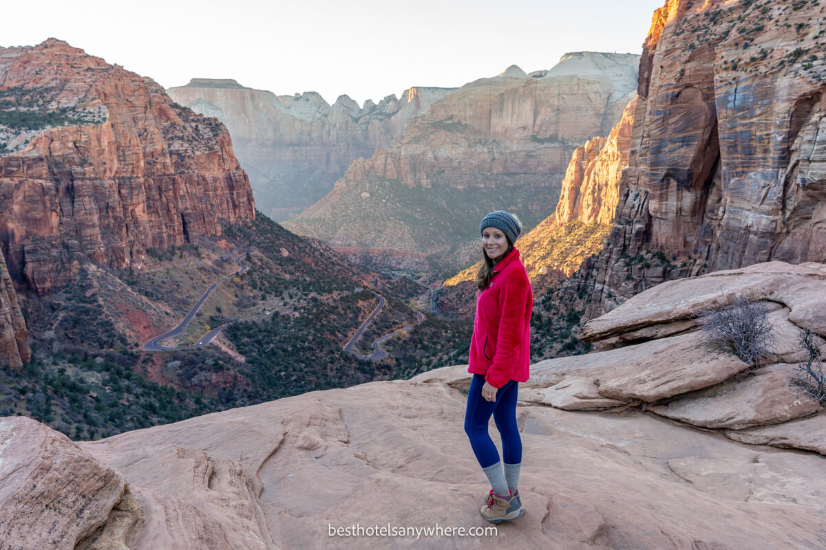Hiker in pink coat stood at the Zion Canyon Overlook summit viewpoint at sunset
