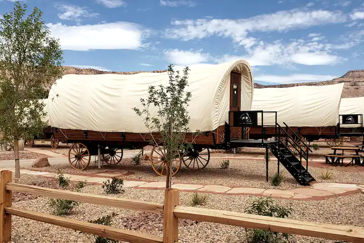 Covered wagons with steps leading inside on gravel with blue sky behind