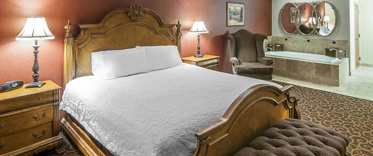 Inside a guest bedroom at a Deadwood SD hotel with large bed on wooden frame and ottoman