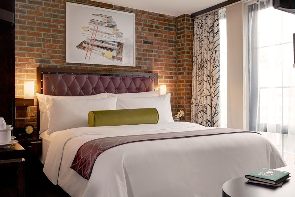 Luxury guest room at the Archer Hotel in Midtown Manhattan with brick wall behind comfy bed
