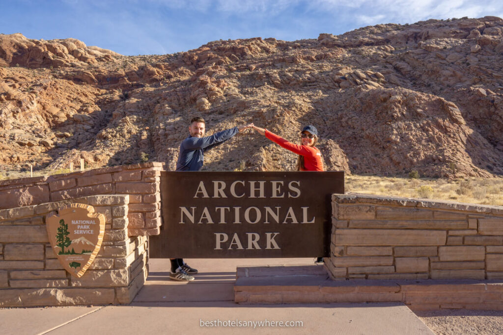Couple forming an arch with arms over the Arches National Park sign in Utah