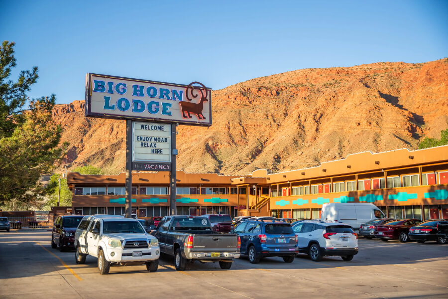 Exterior photo of a motel style hotel in Moab Utah with sign and cars parked in a lot