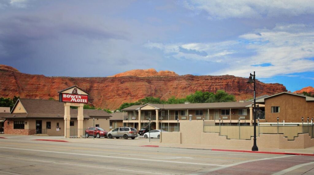 Exterior photo of a motel with red rock formations behind on a cloudy day