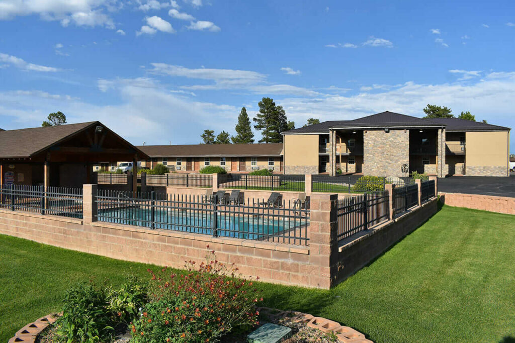 Garden with green grass leading to a swimming pool with stone wall and buildings in Utah