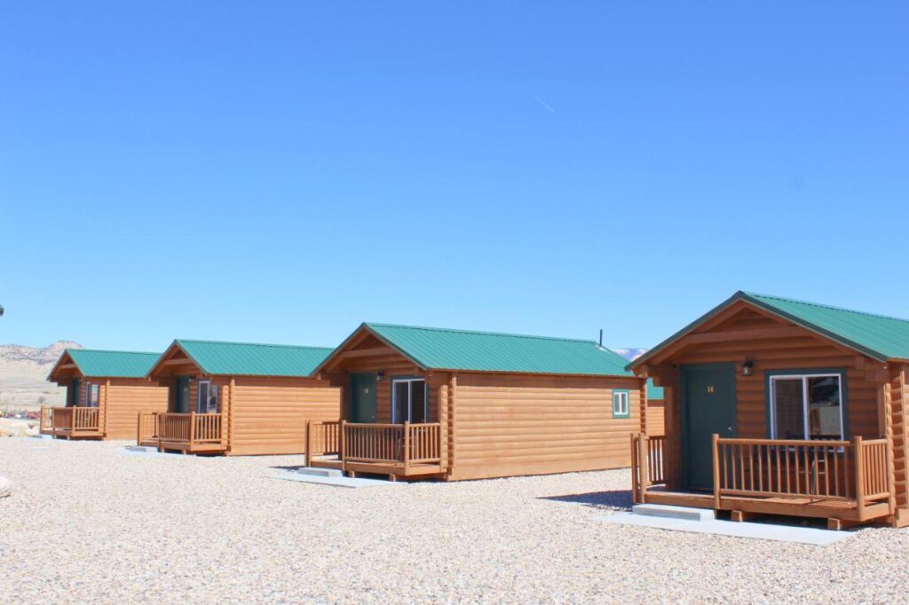Several wooden cabins lined up next to each other on gravel and with a blue sky