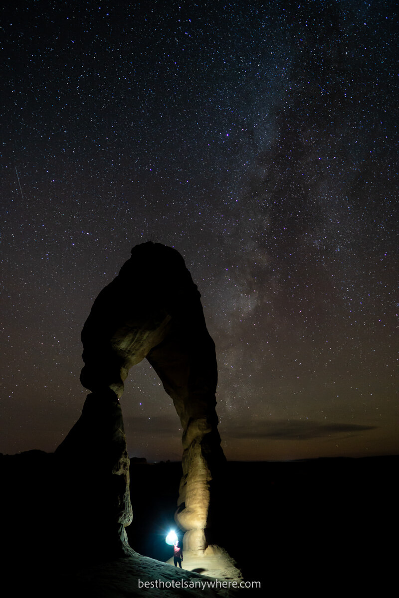 Man stood underneath Delicate Arch with flashlight at night Milky Way