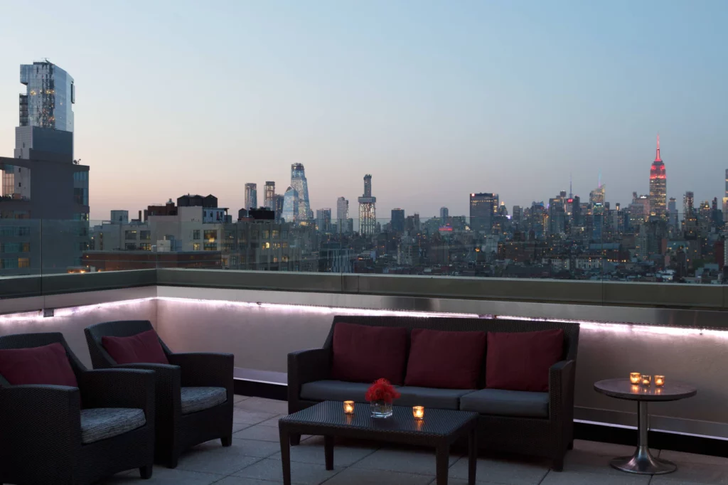 Rooftop bar with chairs and sofas overlooking Midtown Manhattan at dusk