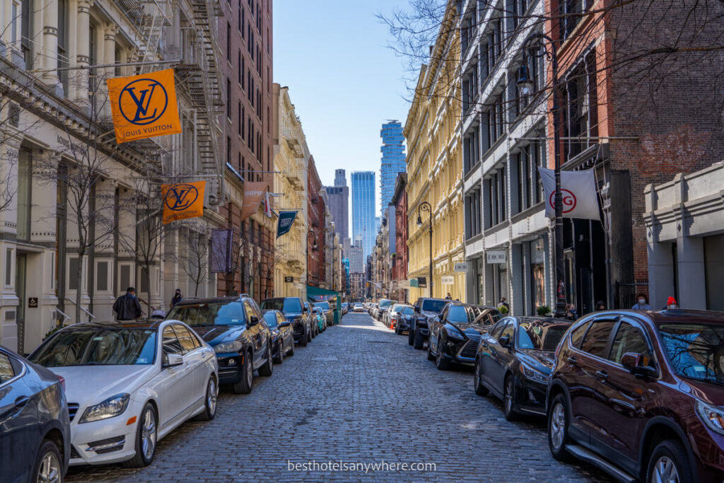 Cobblestone shopping street of SoHo NYC with cars and buildings painted bright colors lining the road