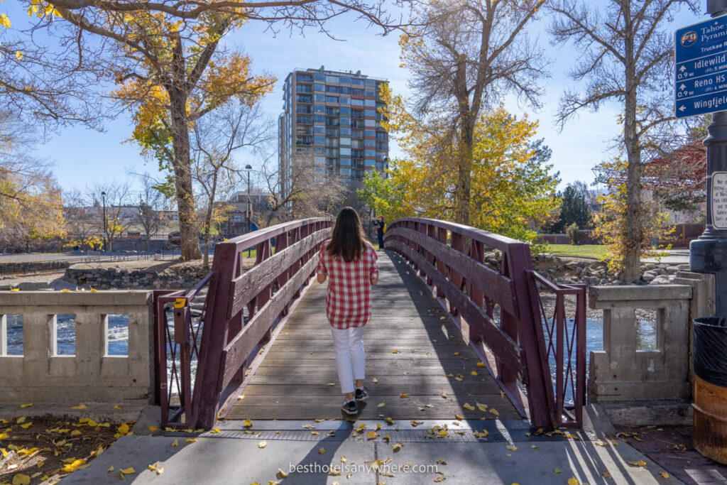 Person walking across a metal bridge with trees over the Truckee River