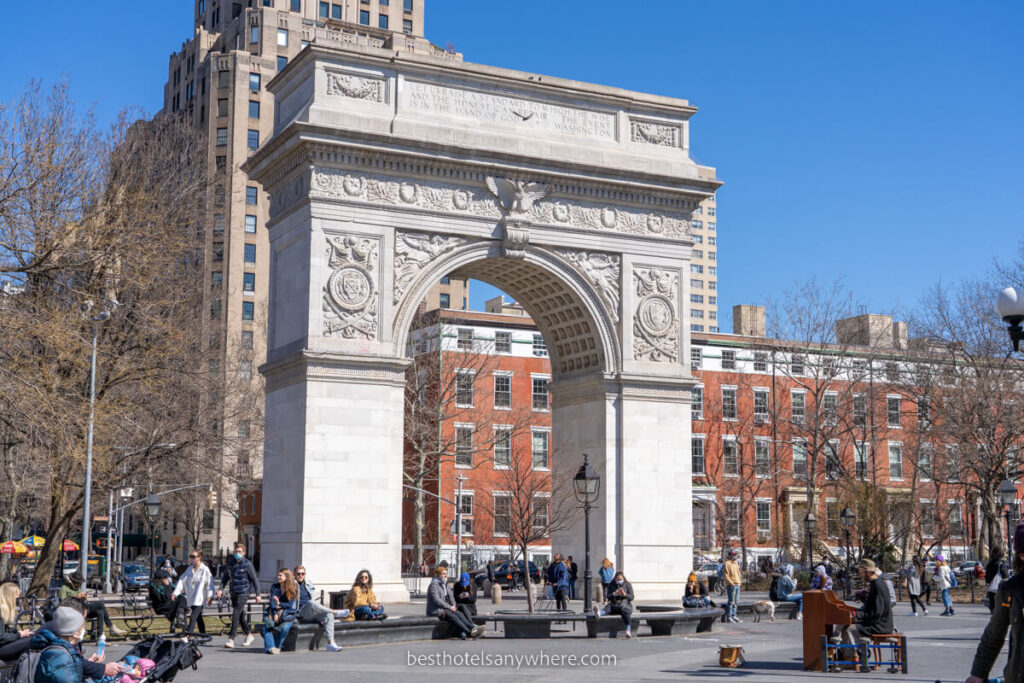 Washington Square Arch with locals and tourists walking around in the park on a sunny day