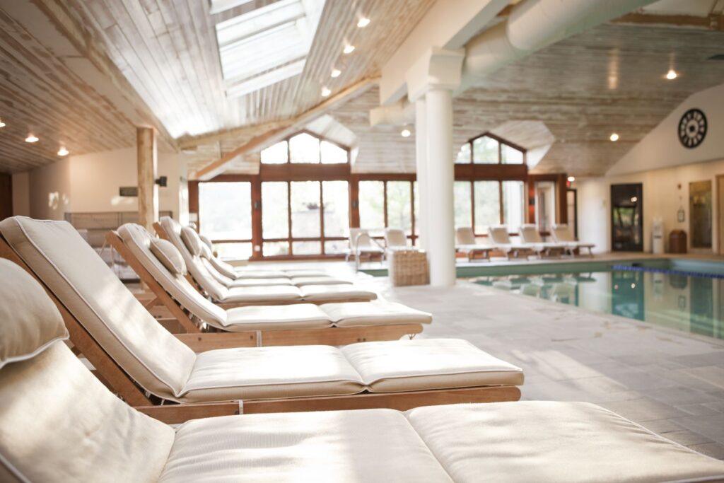 Poolside loungers next to an indoor swimming pool with glass coverings but plenty of light