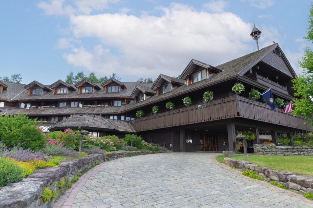 Exterior photo of a multistory wooden lodging structure with road and flowers leading to the entrance
