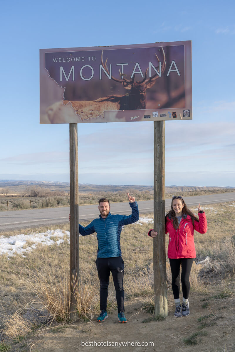 Couple standing underneath a state sign for Montana pointing to the sign